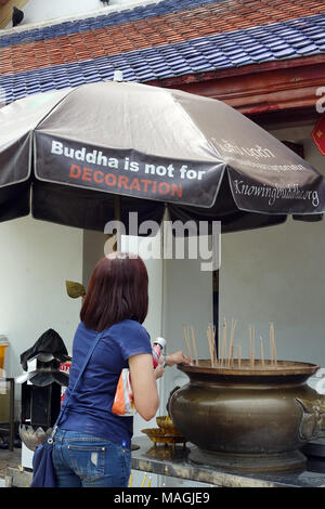 27 février 2018, la Thaïlande, Bangkok : une femme prie au Wat Arun (Temple de l'aube) et allume un encens. Un parasol indique 'Bouddha n'est pas pour la décoration'. Toute la Thaïlande il y a des affiches et des panneaux d'information au sujet d'un traitement respectueux de Bouddha. L'image de l'illuminé n'est pas d'être utilisé comme décoration de pour des raisons commerciales. Photo : Alexandra Schuler/dpa Banque D'Images