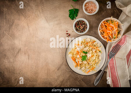 Pilaf de boulgour au poulet dans une assiette et un bol de salade de chou sur un fond brun béton. Vue de dessus, la place pour le texte Banque D'Images