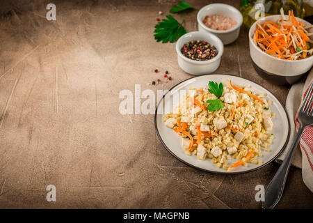 Pilaf de boulgour au poulet dans une assiette et un bol de salade de chou sur un béton fond brun Banque D'Images