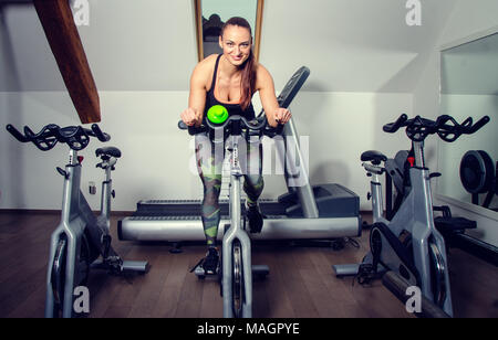 Jeune femme sur un vélo à la salle de sport. Banque D'Images
