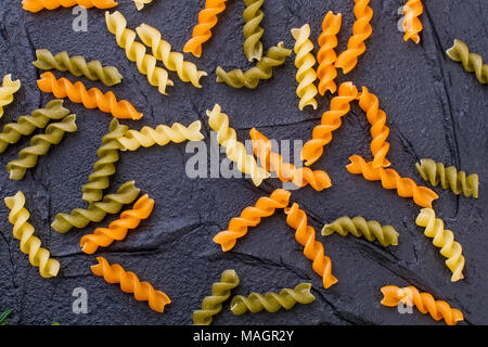 Couleur brut pâtes en spirale sur ardoise. Trois crus fusilli pâtes de blé blé dur de couleur noir ardoise texturé sur. Concept de la cuisine italienne traditionnelle. Banque D'Images