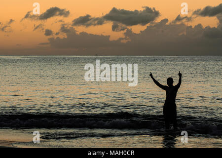 Homme jouant et a mis ses mains dans le ciel au coucher du soleil dans la mer, silhouette concept Banque D'Images