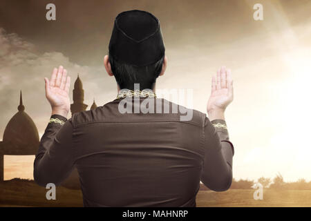 Vue arrière de l'homme musulman d'Asie à l'aide à prier Dieu avec arrière-plan de la lumière du soleil Banque D'Images