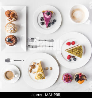 Vue du dessus de l'assemblage de pièces de différents gâteaux sur les assiettes, tasses de café et petits gâteaux isolated on white Banque D'Images