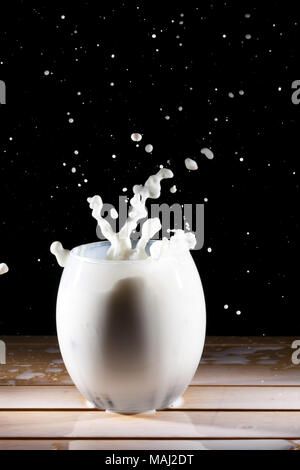 Lait/blanc splash liquide à partir de la table en bois et verre sur fond noir Banque D'Images