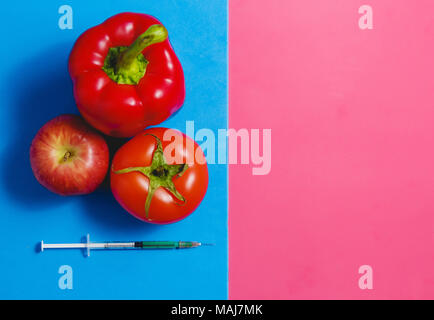 Un liquide vert dans la seringue, tomate, pomme rouge, le poivre. Les aliments modifiés génétiquement Concept sur Rose bleu. Banque D'Images