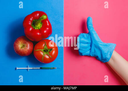 Thumb up un liquide vert dans la seringue, tomate, pomme rouge, le poivre. Les aliments modifiés génétiquement Concept sur Rose bleu. Banque D'Images