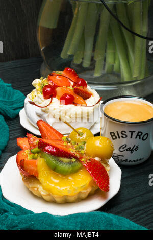 Tulip dans un vase avec une tasse de café et un gâteau aux fruits sur fond sombre. Coffee Time. Cadeau de fleur. Pavlova pie Banque D'Images