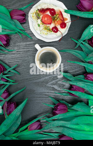 Beau printemps tulipe fraîche avec tasse de café et un gâteau aux fruits sur fond sombre. Coffee Time. Cadeau de fleur. Pavlova pie Banque D'Images