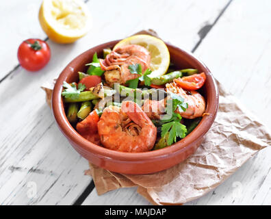 Plaque de tapas frais aux crevettes et asperges vertes, tranche de citron et le persil. Plat gastronomique sur une table en bois blanc. Banque D'Images