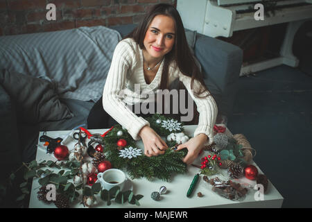 Fleuriste Cute Woman Making Christmas Wreath avec billes de verre, Snowflake et vert Arbre de Noël au bureau à domicile 24. Travail du fleuriste Banque D'Images