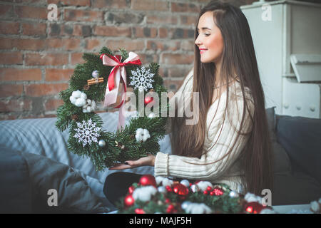 Heureux jeune fleuriste femme assis à la maison de travail et faire de cet arbre de Noël couronne, avec billes de verre rouge, cônes, ruban et la cannelle. Du vrai Banque D'Images