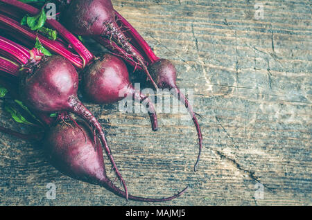 Des tas de jeunes betteraves organiques avec des feuilles vertes sur la table. Les betteraves récoltées fraîches sur fond de bois avec place pour le texte. Style rustique Banque D'Images