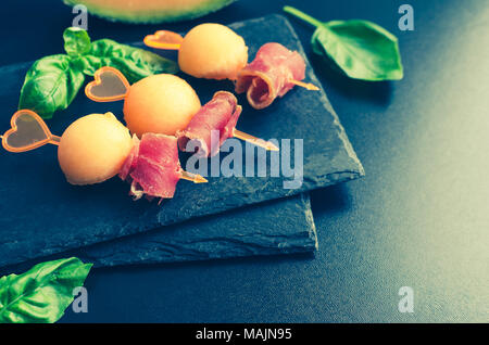 Canape colorés sur les brochettes au melon et prosciutto sur une plaque en ardoise sur fond sombre. Savoureux hors-d pour un parti ou un banquet. Concept de l'italien f Banque D'Images