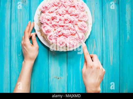 Woman's hands couper le gâteau avec la crème rose sur fond de bois bleu. Gâteau rose. Vue d'en haut Banque D'Images