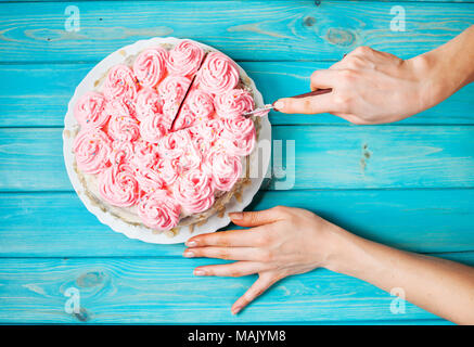 Woman's hands couper le gâteau avec la crème rose sur fond de bois bleu. Gâteau rose. Vue d'en haut Banque D'Images