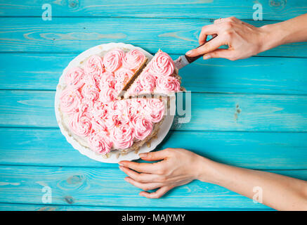 Woman's hands couper le gâteau avec la crème rose sur fond de bois bleu. Gâteau rose. Vue d'en haut Banque D'Images