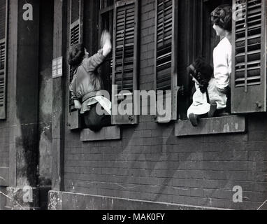 L'horizontale, 1970 Photographie noir et blanc de deux femmes et un bébé dans les fenêtres d'un bâtiment en brique. La femme sur la gauche se lave l'extérieur de la fenêtre que l'autre regarde. Titre : Laver les vitres d'une habitation de Saint-Louis. La chambre Chambres meublées 'offerts' à 'messieurs.". vers 1910. Banque D'Images
