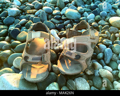 Une paire de sandales en cuir des hommes sur la plage en pierre sous la lumière du soleil près de la mer Banque D'Images