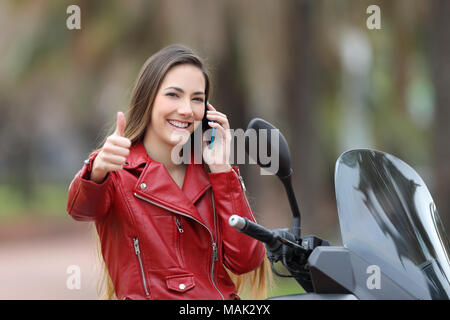 Motards heureux assis sur une moto avec Thumbs up appelant sur le téléphone dans la rue Banque D'Images