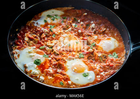 Savoureux et sain Shakshuka, oeufs pochés dans une sauce tomate épicée , poivre dans une poêle, sur fond noir Banque D'Images