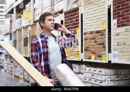 L'homme avec le smartphone choisit et achète des biens dans un supermarché de la construction Banque D'Images