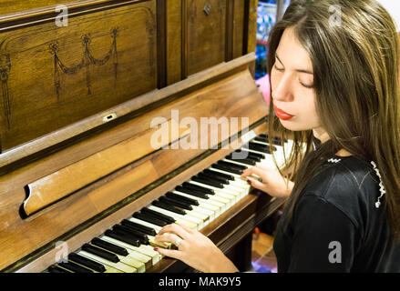 Une jeune femme blonde avec des clous de couleur de la lecture d'un très vieux piano avec touches en ivoire, en regardant avec les yeux fermés. Banque D'Images