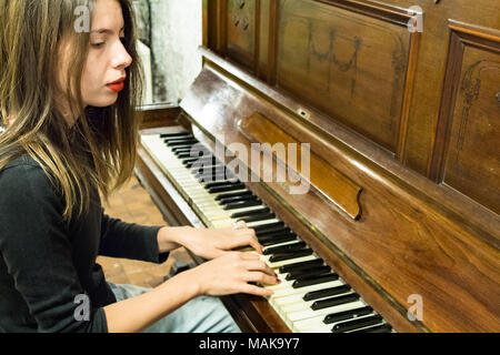 Une jeune femme blonde avec des clous de couleur de la lecture d'un très vieux piano avec des touches d'Ivoire, à la suite, la pensée. Banque D'Images