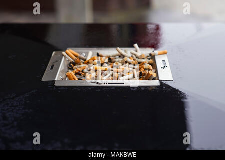 Un cendrier plein sur le dessus d'une poubelle sous la pluie Banque D'Images
