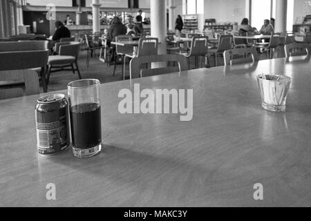 Une canette de cola et de verre dans un café avec du flou en arrière-plan, en noir et blanc granuleux Banque D'Images