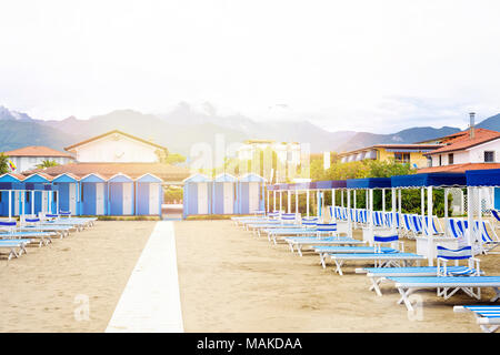 Voir la lumière du jour à bleu chaises longues et des parasols sur la plage. Ciel nuageux, les immeubles et les montagnes de l'arrière-plan. Copie négative de l'espace, place pour le texte Banque D'Images