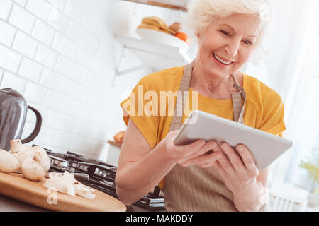 Pensionné woman holding tablet, regardant la vidéo ou lisez le livre dans l'internet. Piscine, studio tournage, cuisine intérieur Banque D'Images