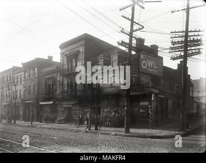 À l'horizontal, photographie en noir et blanc d'un coin de rue avec avec un petit groupe d'hommes et de garçons debout autour sur le trottoir. La pharmacie près de l'angle a un signe de langue allemande dans la fenêtre 'Apotheke" (pharmacie). Titre : Broadway et Park, coin sud-ouest. . Vers 1905. Oscar Kuehn Banque D'Images