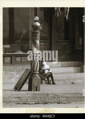 Vertical, photographie noir et blanc montrant une jeune fille tenant un bébé sur ses genoux sur l'abaisse d'un barber shop non identifiés. Un salon de coiffure en bois peint la perche avec rayures et fleurs de lis peut être vu dans l'avant-plan. Titre : Une jeune fille tenant un bébé sur ses genoux sur l'abaisse d'un barber shop non identifiés. . Vers 1910. Holt, Charles Clement, 1866-1925 Banque D'Images