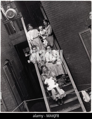 Vertical, photographie noir et blanc montrant des femmes et des enfants assis à l'arrière de l'étapes d'un tenement St Louis non identifiés. Une femme tient un petit chien alors qu'un autre chien est assis à ses pieds. L'escalier traverse le centre de l'image. Une fenêtre avec des volets peut être vu sur la gauche, tandis qu'un mur de brique se trouve sur la droite. L'entrée d'un appartement peut être vu en haut de l'escalier, et une grande casserole ou bassine pend du petit palier. Titre : Les femmes et leurs enfants se réunissent sur les étapes d'une arrière St Louis non identifiés tenement. . Entre 1900 et 1910. Holt, Charles Clement, 1 Banque D'Images