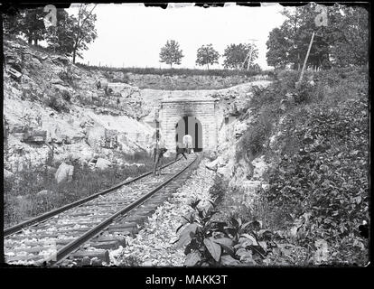 L'horizontale, 1970 Photographie noir et blanc montrant deux hommes avec des caméras positionnées sur les voies ferrées à côté d'un tunnel. Un photographe a la caméra sur son épaule et fait face à l'observateur. L'autre photographe a son retour à la visionneuse et est en train de prendre une photo du tunnel. Un adulte et l'enfant sont debout près de l'entrée du tunnel. Rocks et le feuillage peut être vu sur l'autre côté de la voie et au-dessus du tunnel. Titre : Les photographes sur les voies à la Highlands Meramec Tunnel. . 1895. Banque D'Images