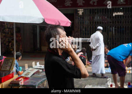 31.03.2018, Singapour, République de Singapour, en Asie - Un homme boit à partir d'une bouteille comme il parle au téléphone à un petit marché aux puces dans le quartier chinois. Banque D'Images