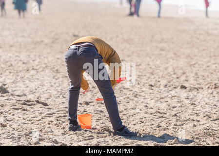 La vue arrière d'un homme penché au-dessus et faire des châteaux de sable avec un seau et la cosse sur la plage de Fistral, Newquay Cornwall Banque D'Images