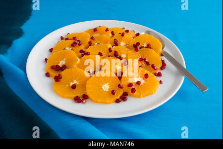 Salade d'orange et de grenade arrosées de miel d'acacia sur une grande assiette de porcelaine blanche avec une cuillère de service. Banque D'Images