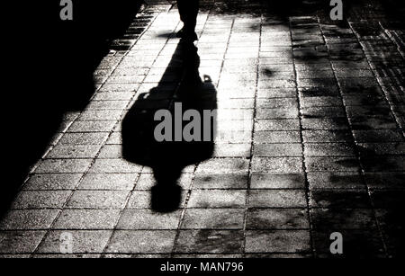 Ombre floue et silhouette d'un homme debout, dans la nuit, sur le trottoir de la rue ville humide avec de l'eau reflet en noir et blanc Banque D'Images