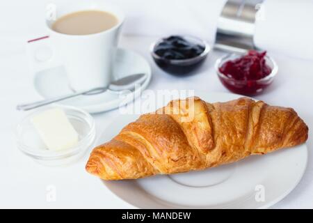 Petit-déjeuner croissant servi avec des confitures, du beurre et une tasse de café avec du lait Banque D'Images