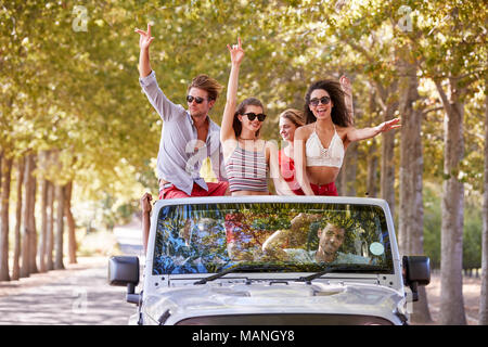 Les amis s'amusant debout dans l'arrière d'une voiture à toit ouvert Banque D'Images