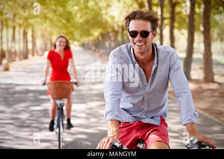 Les jeunes adultes blanc couple riding bikes sur une calme route ensoleillée Banque D'Images