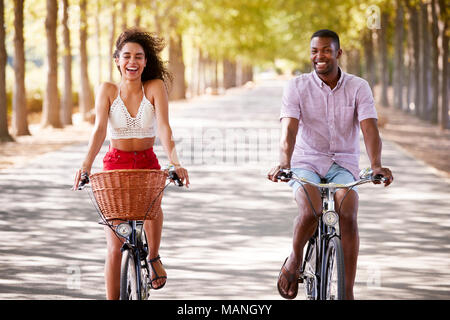 Young caucasian couple riding bicycles sur une route bordée d'arbres Banque D'Images