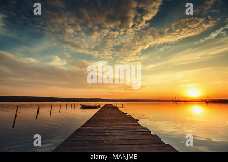 Jetée en bois et en bateau sur le lac avec un reflet dans l'eau au coucher du soleil Banque D'Images