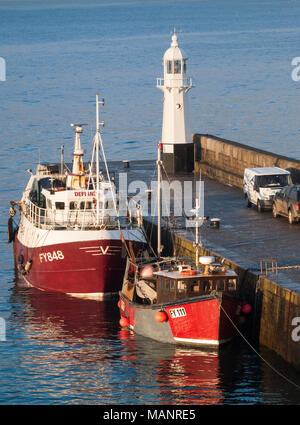 Les bateaux de pêche amarrés par l'Mivagissey Pier, le phare en arrière-plan. Banque D'Images