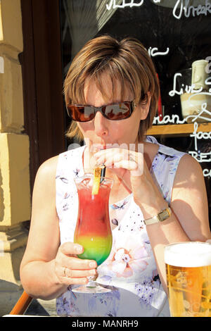 Femme / Femme assise à l'extérieur, au soleil au café un bar bénéficiant d''un cocktail coloré de boire avec une paille dans la ville de Budapest, Hongrie Banque D'Images