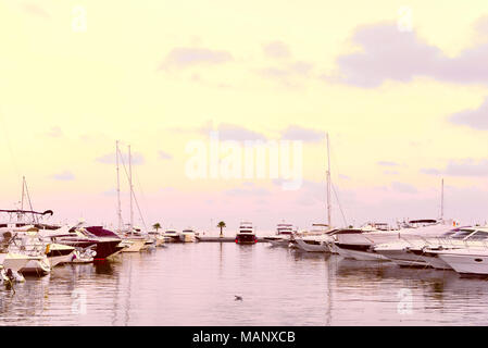 Port de plaisance dans la soirée avec de luxueux voiliers et bateaux à moteur à l'ancre. Scène Marina dans le coucher du soleil. Banque D'Images