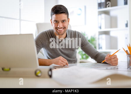 Les jeunes hommes d'analyser constructeur plan at desk in office. En regardant la caméra. Banque D'Images