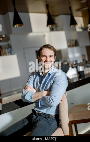 Smiling musclé brun personne assise sur la chaise avec les bras croisés Banque D'Images